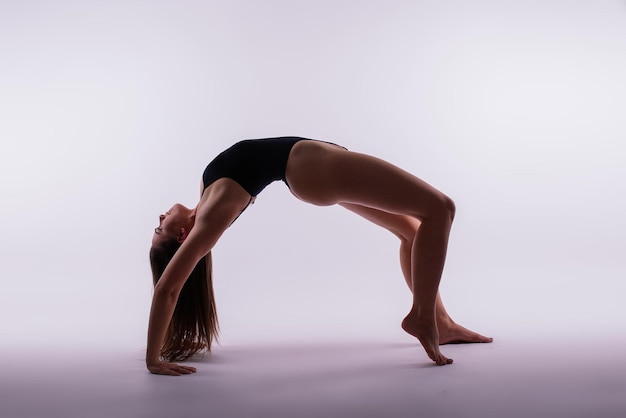 Retrato de una hermosa joven con ropa deportiva negra haciendo ejercicio en el estudio de cuerpo entero