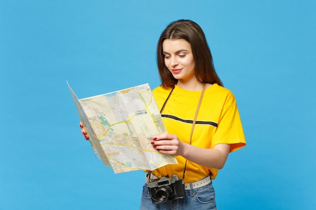 Retrato de una hermosa joven con ropa informal vívida con una cámara de fotos retro vintage con un mapa de la ciudad de papel aislado en el fondo de la pared azul en el estudio. Concepto de estilo de vida de las personas. Simulacros de espacio de copia.