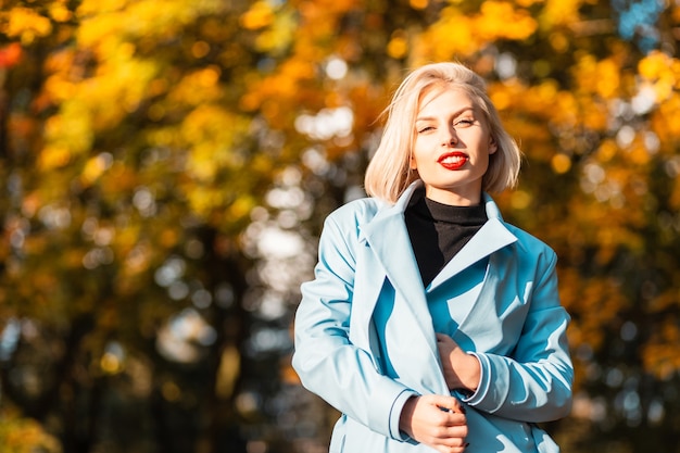 Retrato de una hermosa joven rubia con labios rojos sobre un fondo de hojas de otoño coloridas amarillas en un día soleado de otoño