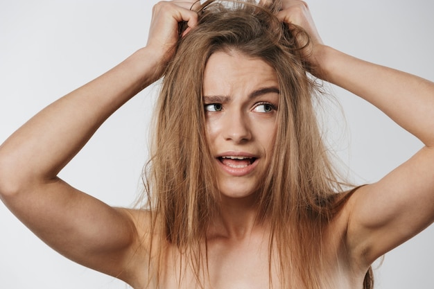 Retrato de hermosa joven rubia semidesnuda tocando su cabello desordenado aislado en blanco