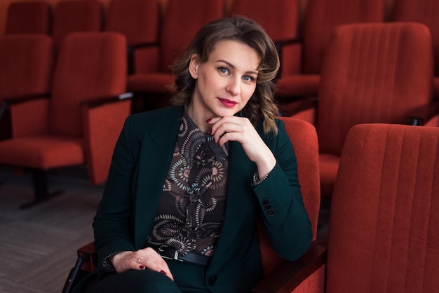 Retrato de una hermosa joven sentada en asientos de terciopelo en la sala de conferencias o en el teatro mirando a la cámara