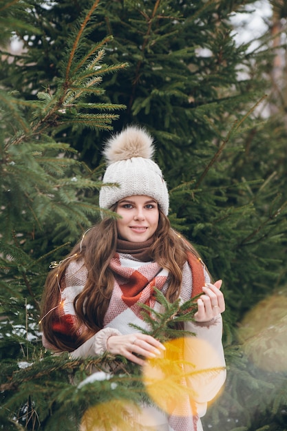 Retrato de una hermosa joven con un sombrero entre árboles de Navidad de invierno con luces. Un parque con árboles de Navidad al fondo. Humor navideño. Tintes.