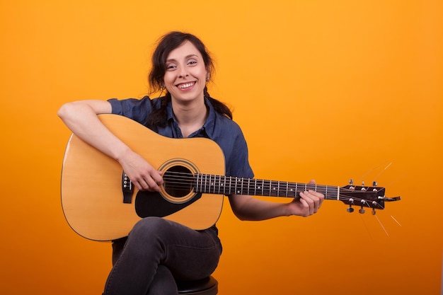 Retrato de una hermosa joven sonriendo en un estudio con guitarra sobre un fondo amarillo. Mujer bastante joven músico. Joven artista femenina. Mujer alegre con instrumento musical.