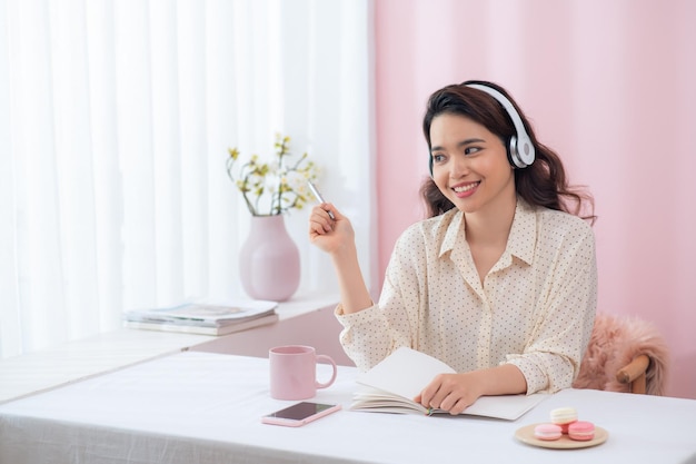 Retrato de una hermosa joven sonriente feliz sentada en la oficina escuchando música con auriculares
