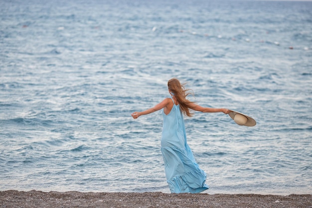 Retrato de una hermosa joven sonriente con sombrero de paja en la playa con el mar de fondo Chica de moda de belleza mirando a la cámara en la playa Mujer bronceada despreocupada caminando sobre la arena y riendo
