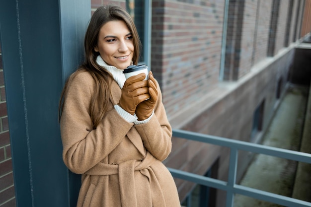 Retrato de una hermosa joven con una taza de café caliente en la mano al aire libre