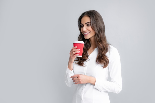 Retrato de una hermosa joven con una taza de café parada en el fondo gris