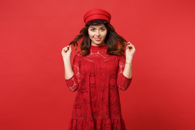 Retrato de una hermosa joven con vestido de encaje y gorra sosteniendo una cámara con aspecto de pelo aislada en un fondo de pared rojo brillante en el estudio. Emociones sinceras de la gente, concepto de estilo de vida. Simulacros de espacio de copia.