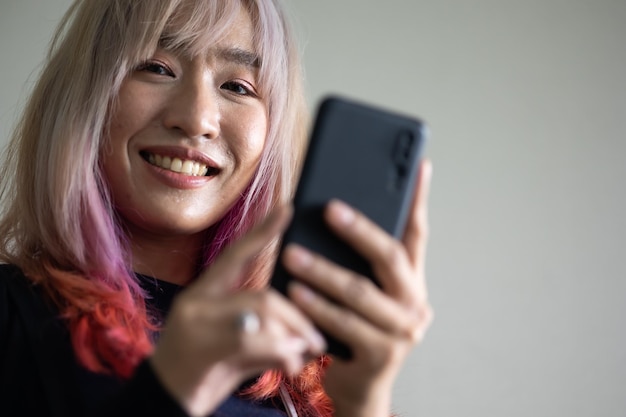 Retrato de una hermosa modelo asiática elegante y moderna que usa un teléfono inteligente con ropa informal de verano rosa pastel y cabello rojo