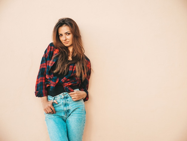 Retrato de hermosa modelo. Mujer vestida con jeans y camisa a cuadros de verano hipster. Chica de moda posando junto a la pared en la calle