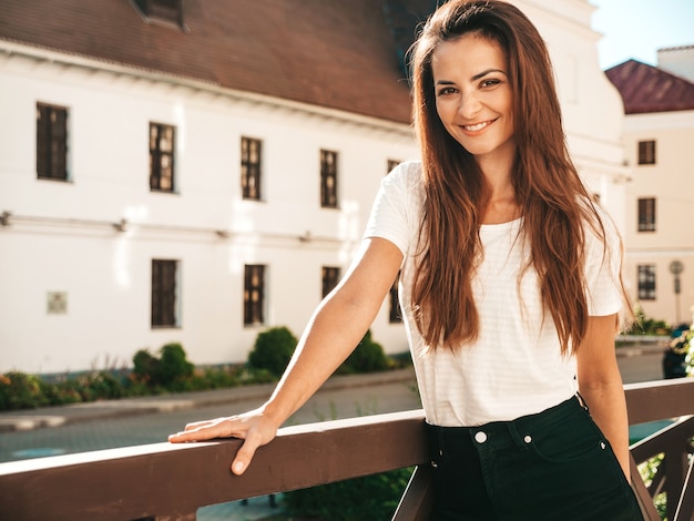 Retrato de hermosa modelo sonriente. mujer vestida con jeans y camiseta blanca de verano hipster. chica de moda posando junto a la pared en la calle