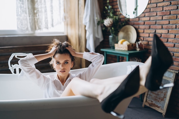 Retrato de una hermosa morena acostada en un baño vacío sosteniendo las piernas