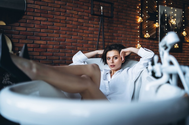 Retrato de una hermosa morena acostada en un baño vacío sosteniendo las piernas