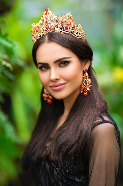 Foto retrato de una hermosa morena con una corona roja parada en un jardín con fondo verde