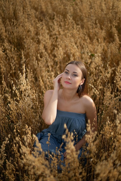 Retrato de una hermosa morena con un vestido azul en un campo amarillo con trigo en el pueblo