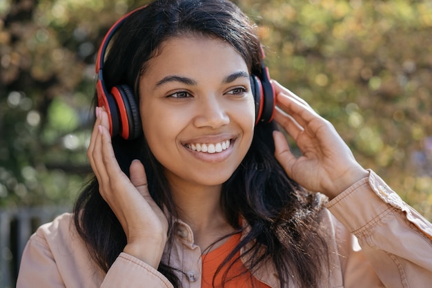 Retrato de hermosa mujer afroamericana escuchando música en auriculares, sonriendo