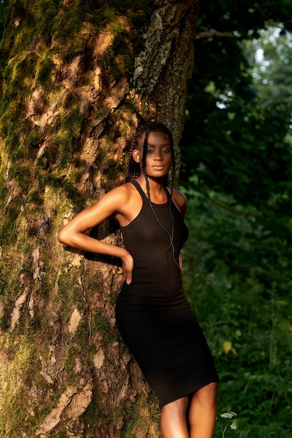 Retrato de hermosa mujer afroamericana de pie en el bosque cerca de árboles