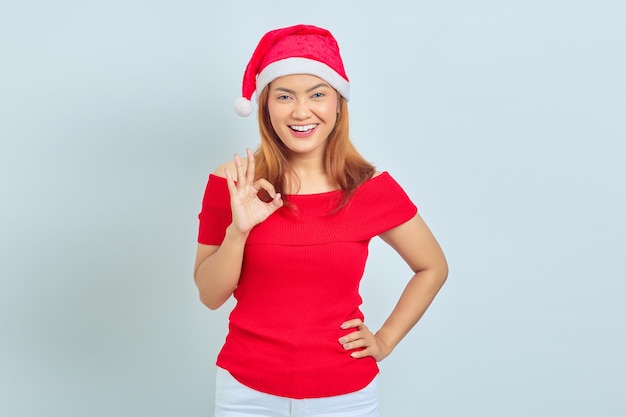 Retrato de hermosa mujer asiática alegre con vestido de Navidad y mostrando gesto ok sobre fondo blanco.