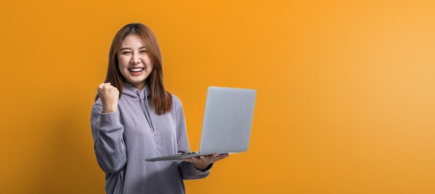 Retrato de una hermosa mujer asiática haciendo una pose alegre y sosteniendo una laptop en un concepto de retrato de fondo aislado utilizado para publicidad y señalización aislada sobre el espacio de copia de fondo amarillo