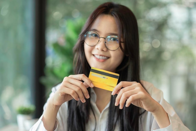 Retrato de una hermosa mujer asiática joven que muestra una tarjeta de crédito para transacciones de comercio electrónico en línea pago de préstamos de devolución de dinero compras de deuda