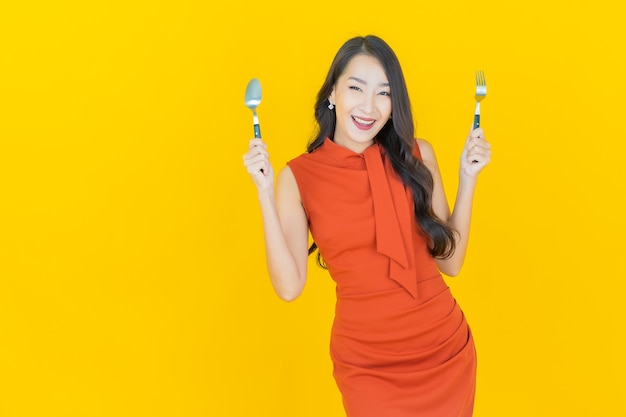 Retrato hermosa mujer asiática joven sonrisa con cuchara y tenedor en amarillo