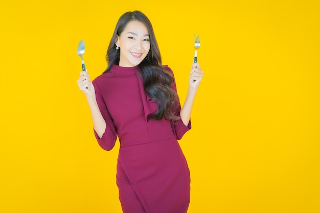 Retrato hermosa mujer asiática joven sonrisa con cuchara y tenedor en amarillo