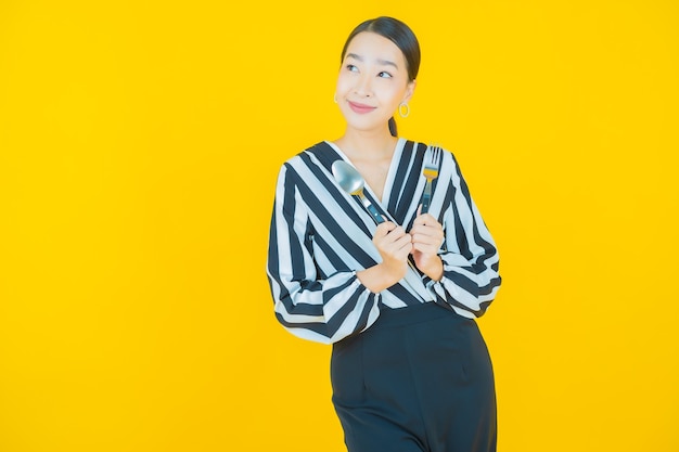 Retrato hermosa mujer asiática joven sonrisa con cuchara y tenedor en amarillo