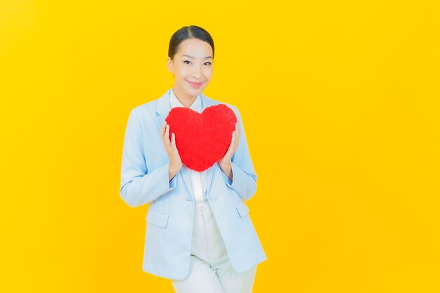 Retrato hermosa mujer asiática joven sonrisa con forma de almohada de corazón en amarillo