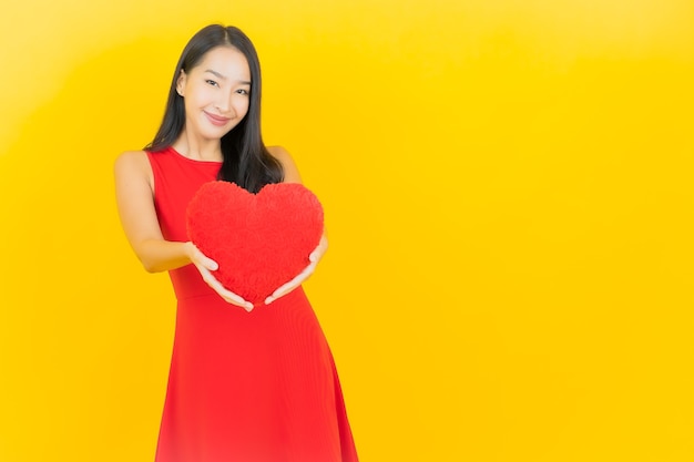 Retrato hermosa mujer asiática joven sonrisa con forma de almohada de corazón en la pared amarilla