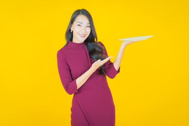 Retrato hermosa mujer asiática joven sonrisa con plato plato vacío en amarillo