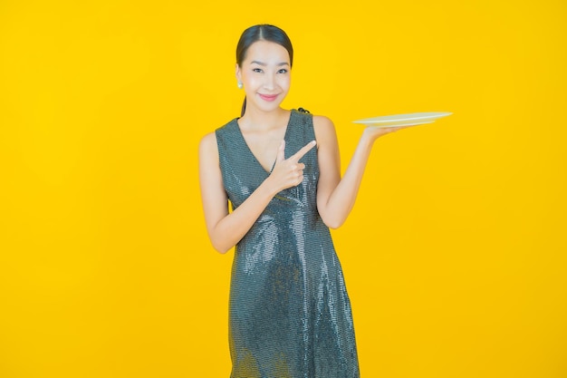 Retrato hermosa mujer asiática joven sonrisa con plato plato vacío en amarillo