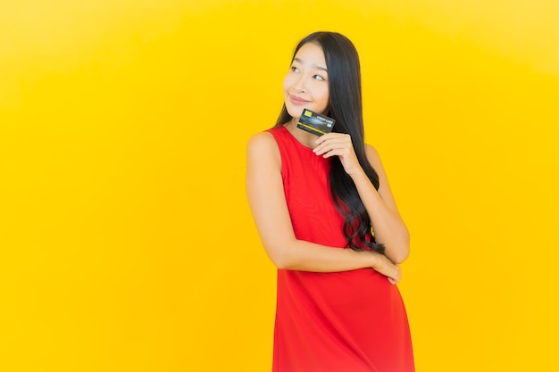 Retrato hermosa mujer asiática joven sonrisa con tarjeta de crédito en la pared amarilla