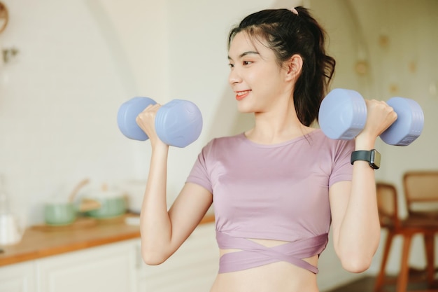 Retrato de una hermosa mujer asiática que usa ejercicio deportivo con pesas en el interior de su casa