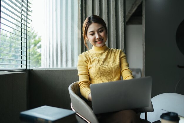 Retrato de una hermosa mujer asiática sentada en un restaurante de cafetería durante el verano usando una tecnología inalámbrica inteligente, una computadora portátil y un teléfono inteligente, descansando en un café.