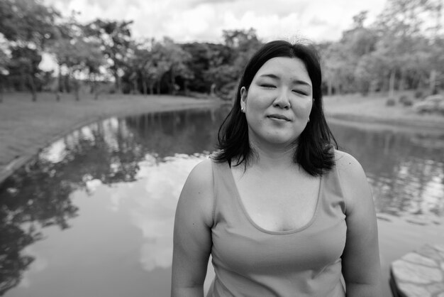 Retrato de hermosa mujer asiática con sobrepeso relajante en el parque de la ciudad en blanco y negro