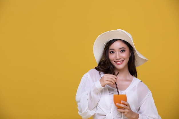 Retrato de hermosa mujer asiática con sombrero sosteniendo un vaso de jugo de naranja