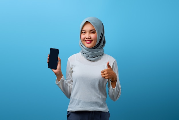 Retrato de hermosa mujer asiática sosteniendo smartphone y mostrando los pulgares para arriba