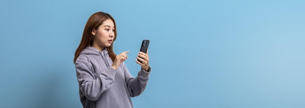 Retrato de una hermosa mujer asiática sosteniendo un teléfono móvil en un concepto de retrato de fondo aislado utilizado para publicidad y señalización aislado sobre un espacio de copia de fondo azul