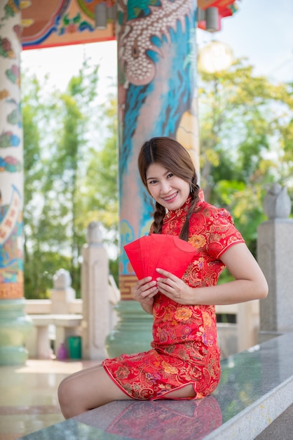 Retrato de hermosa mujer asiática en vestido Cheongsam con sobre rojo en la manoGente de TailandiaFeliz concepto de año nuevo chino