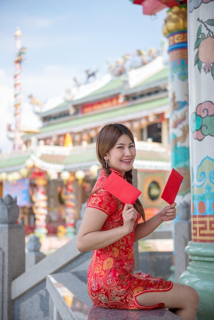 Retrato de hermosa mujer asiática en vestido Cheongsam con sobre rojo en la manoGente de TailandiaFeliz concepto de año nuevo chino