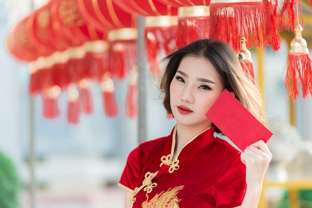 Retrato hermosa mujer asiática en vestido CheongsamGente de TailandiaFeliz concepto de año nuevo chinoFeliz dama asiática en vestido tradicional chino sosteniendo un sobre rojo