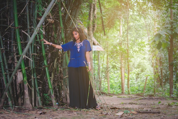 Retrato de hermosa mujer asiática con vestido local, de pie bajo el árbol de bambú en el bosque en el país