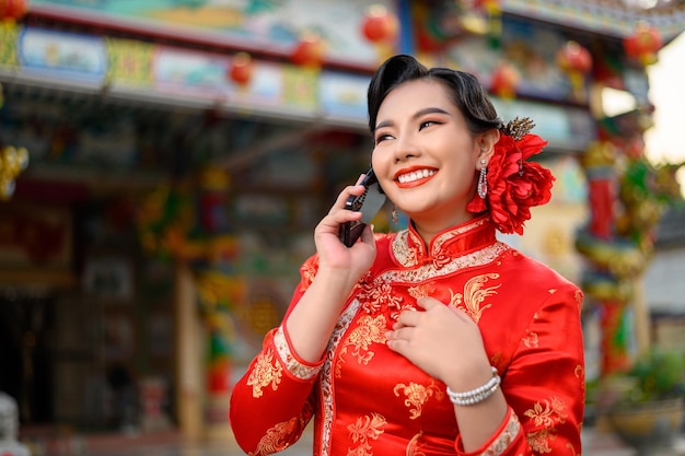 Retrato de hermosa mujer asiática vistiendo un cheongsam sonriendo y usando el teléfono inteligente en el santuario en el año nuevo chino