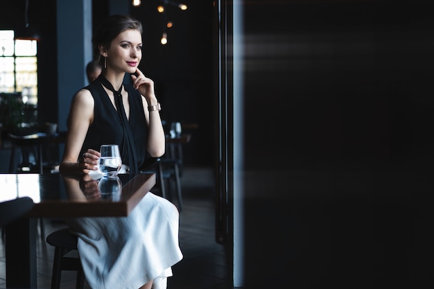 Retrato de hermosa mujer bebiendo té o café y mirando con una sonrisa por la ventana de la cafetería mientras disfruta de su tiempo libre, agradable almuerzo de mujer de negocios en la cafetería moderna durante su descanso laboral.