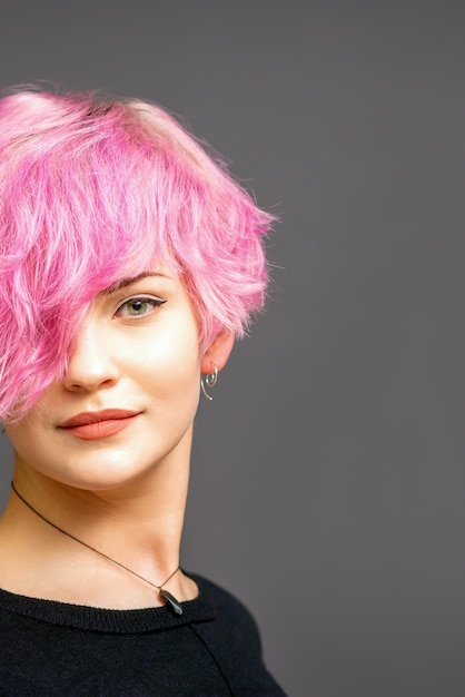 Retrato de hermosa mujer blanca joven con un peinado corto rosa sobre fondo oscuro