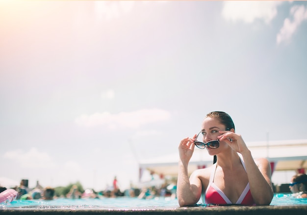 Retrato de hermosa mujer bronceada en traje de baño blanco relajante en el spa de la piscina. Día caluroso de verano y luz brillante y soleada.