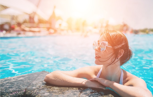 Retrato de hermosa mujer bronceada en traje de baño blanco relajante en el spa de la piscina. Día caluroso de verano y luz brillante y soleada.