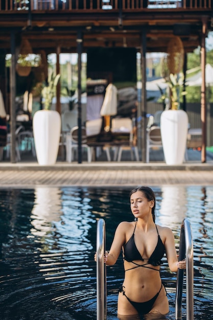 Retrato de hermosa mujer bronceada en traje de baño negro relajante en el spa de la piscina