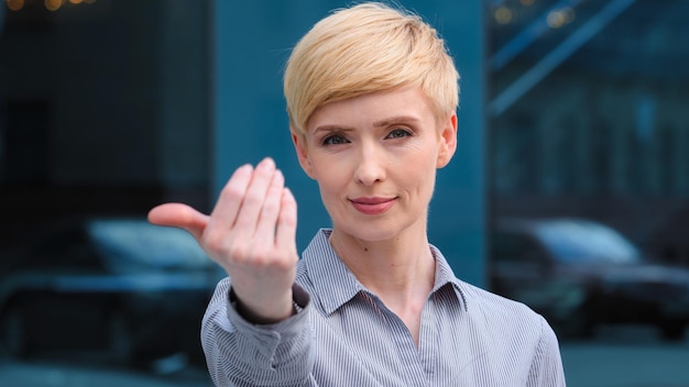 Retrato de una hermosa mujer caucásica adulta de mediana edad de 40 años, una mujer de negocios, una dama amable que sonríe mostrando un gesto de consejo de invitación para acercarse a sí misma con la mano y pide salir al aire libre lenguajes corporales