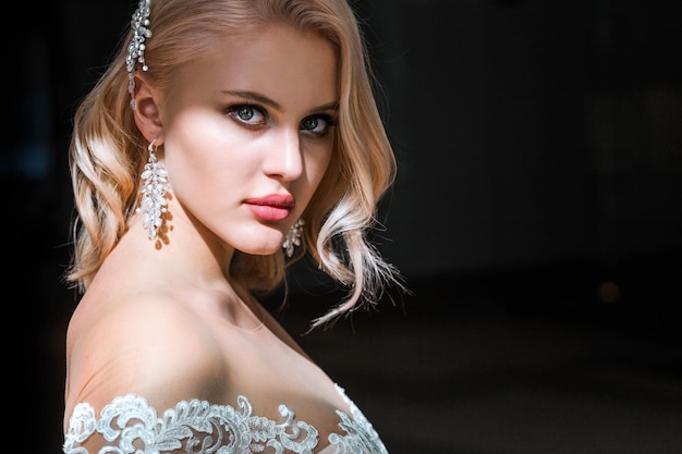 Retrato de una hermosa mujer caucásica con maquillaje de boda y peinado posando en una habitación de hotel con un elegante vestido blanco